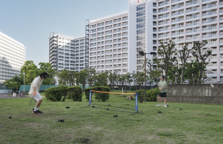 Rasenfläche mit einem Tennisnetz, im Hintergrund Hochhäuser